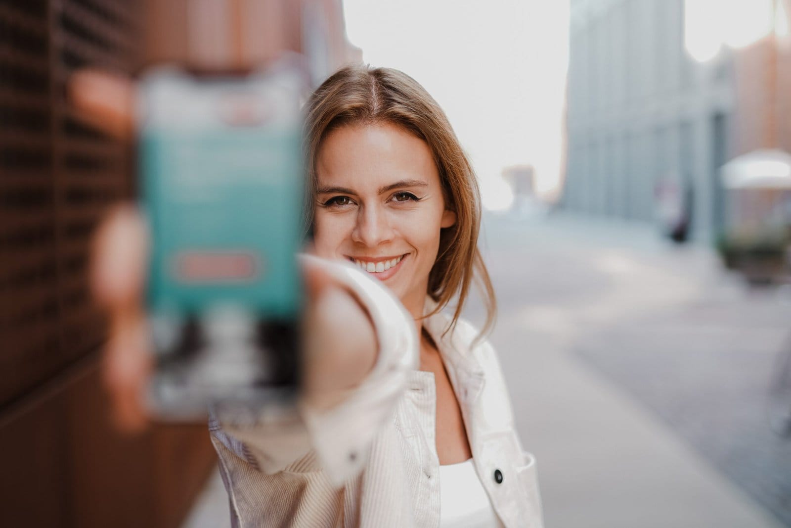 Kuvassa nainen ojentaa älypuhelinta pitelevää kättä kohti kameraa ja hymyilee