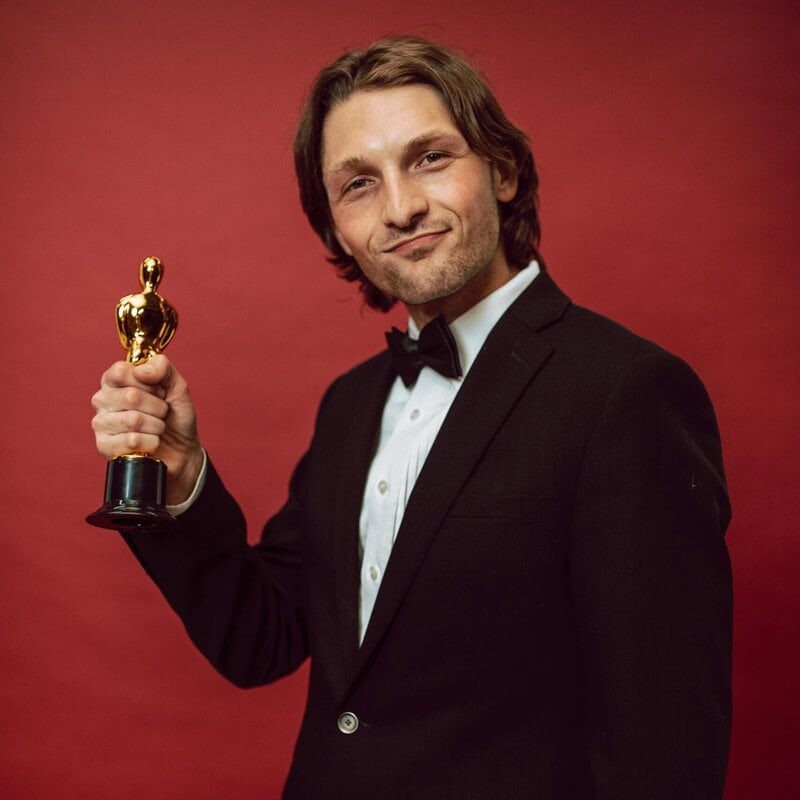 A man in formal attire proudly holds a trophy against a red background, symbolizing success and recognition.